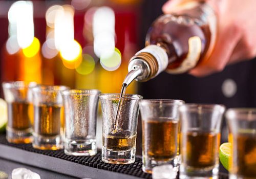 Barman pouring hard spirit into glasses in detail